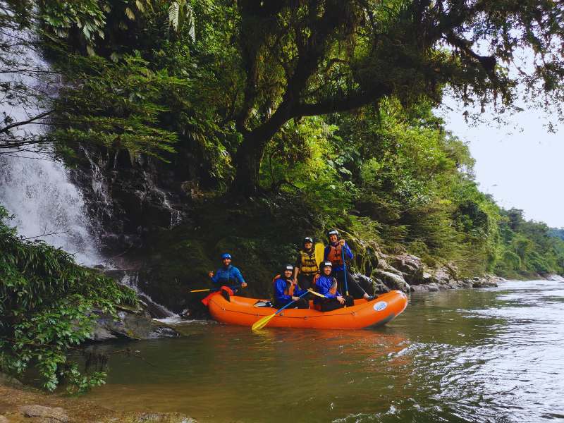 A group of adventurers rafting on an Amazon river surrounded by lush jungle and a waterfall.